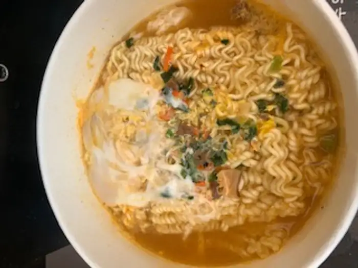 Schale mit Han-River-Ramen – Shin-Ramyun-Instant-Nudeln in Papierschale mit Ei obendrauf, gegessen am Flussufer