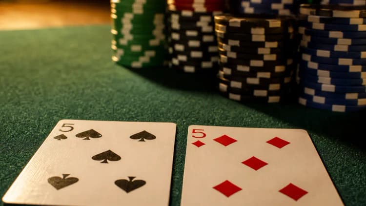 A small pocket pair of fives beside a deep stack of chips on green felt — the setup for a set-mining call that only pays off when stacks are deep
