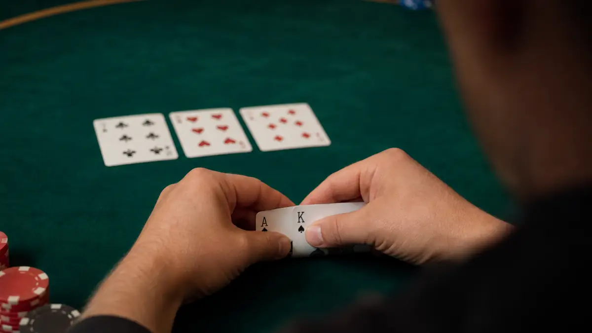 Ein Spieler hält Pik-Ass und Pik-König und studiert einen niedrigen Drei-Karten-Flop auf grünem Filz, während er vor dem Handeln Overcard-Outs zählt