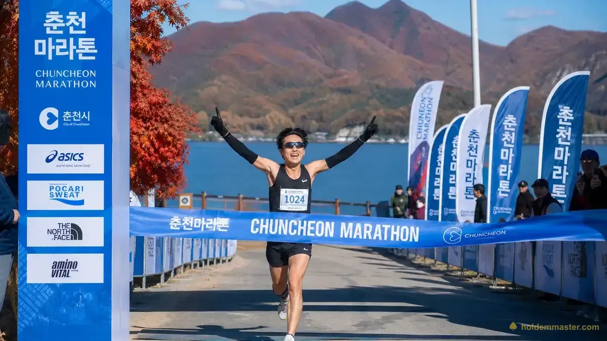 Läufer überquert die Ziellinie in Chuncheon mit Herbstlaub und dem Uiam-See im Hintergrund – Korea Marathon 2026