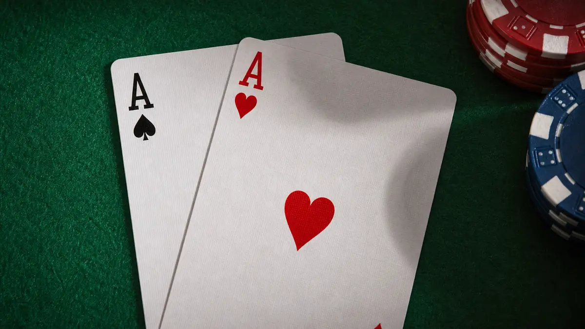 Pocket aces — the ace of spades and ace of hearts freshly dealt on green felt beside poker chips